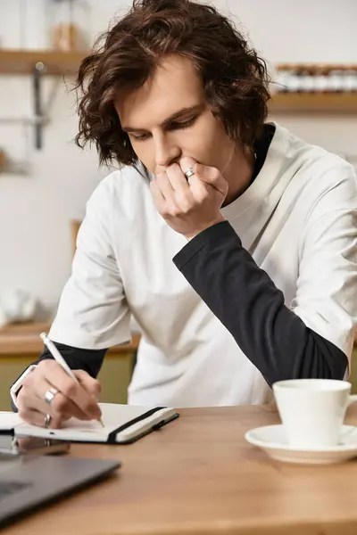 A young man in casual clothing engages in deep thought, writing in a notebook at home. — Stock Photo