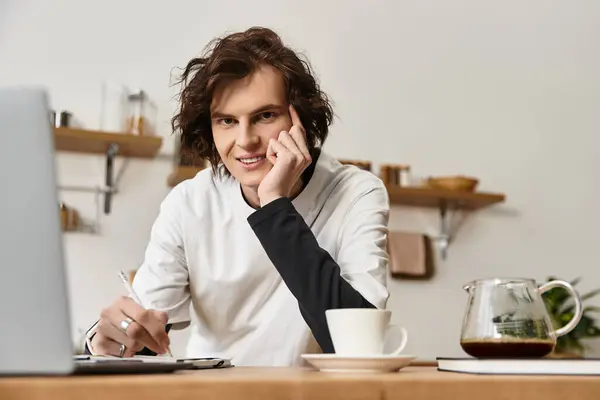 A young man sits at a wooden table, engaged in work, with coffee close by in a serene home setting. — Photo de stock