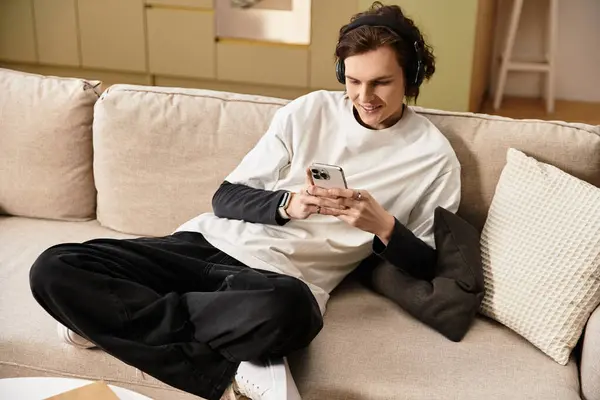 A young man in comfy attire relaxes on a couch, engrossed in his phone, enjoying leisure time. — Stock Photo