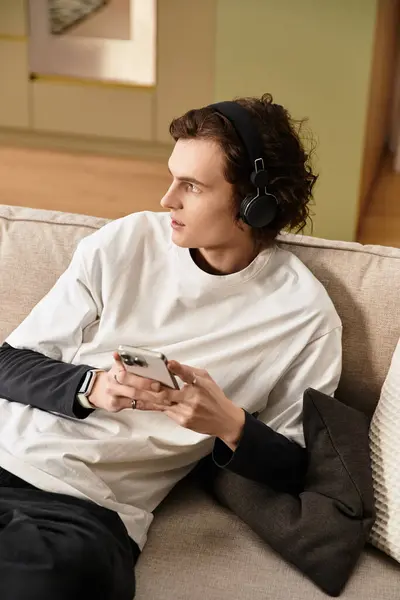 In a warm and inviting living space, a young man relaxes on a couch while listening to music. — Stock Photo