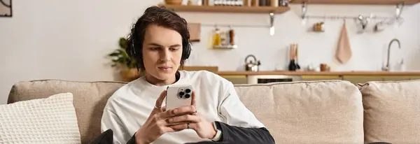 Relaxed young man dressed comfortably engages with his smartphone in a warm home environment. - foto de stock