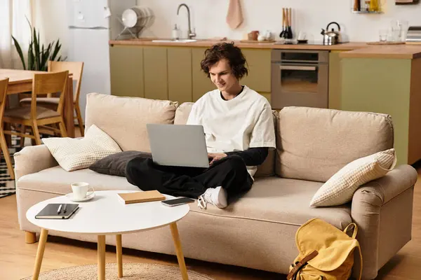 Young man comfortably sitting on sofa, focused on laptop while enjoying a calm home environment. — Fotografia de Stock