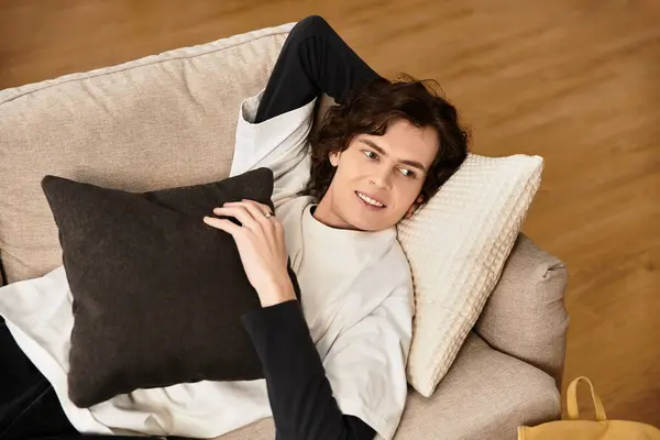 A young man lounges on his sofa, holding a pillow and wearing casual home attire. — Fotografia de Stock