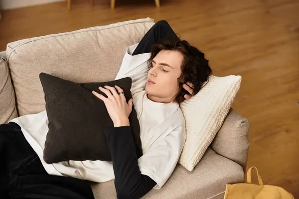 A young man lounges comfortably on a soft couch, cherishing cozy vibes while holding a cushion. — Stock Photo
