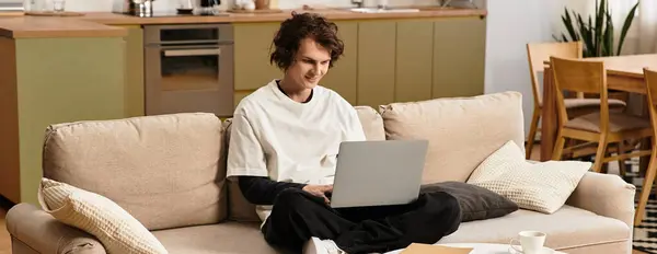 A young man sits comfortably on a couch, focused on his laptop, in a relaxed home setting. — Stock Photo