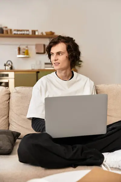 A young man relaxes on the couch in cozy clothes, focused on his laptop. — Stock Photo