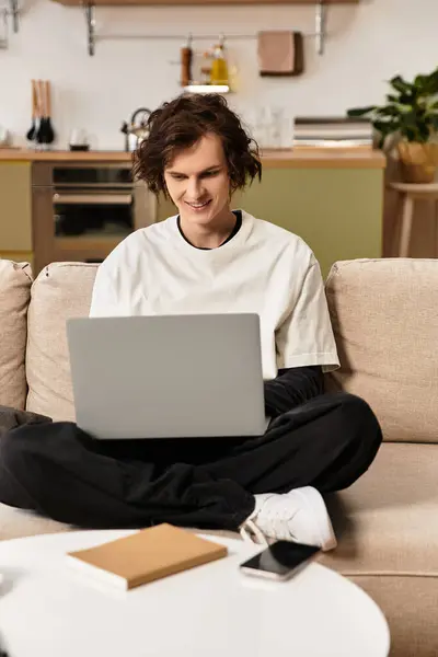 Young man sits cross legged on the couch, engaged with his laptop in a warm home setting. — Stock Photo
