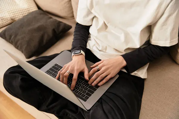Young man dressed in cozy clothes sits relaxed on a sofa, focused on his laptop work. — Fotografia de Stock