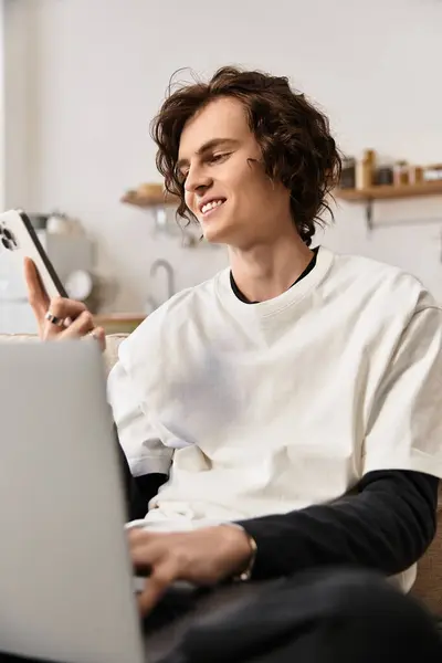 Young man in casual clothing smiles while using his smartphone at home, surrounded by comfort. — Foto stock