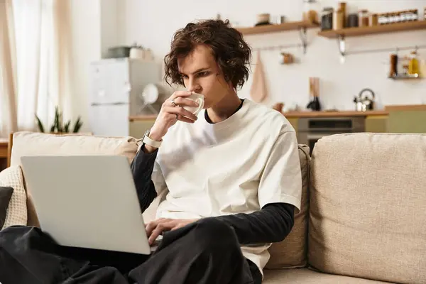 Young man in comfortable clothing focuses on his laptop while sipping coffee at home. — Stock Photo