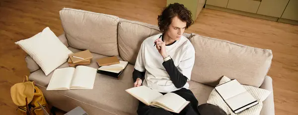 A young man sits comfortably on his couch, immersed in writing and reflecting on his thoughts. — Stock Photo