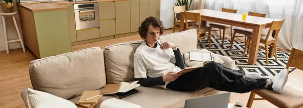 Young man relaxes on the couch, deeply engaged in his thoughts with a notebook in hand. — Stock Photo