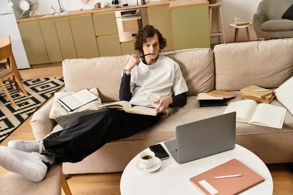 Young man relaxes in his cozy home, deeply engaged in reading and writing while enjoying coffee. — Fotografia de Stock