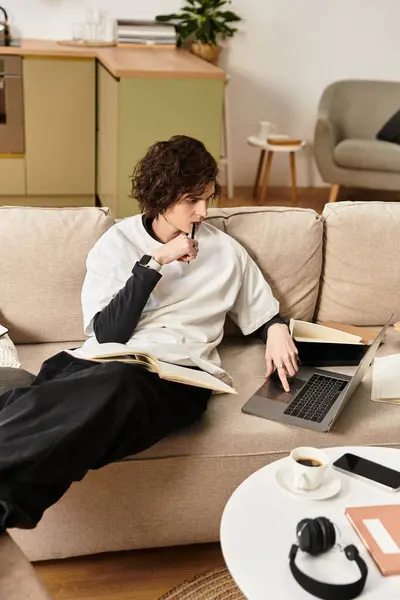 A young man dressed comfortably engages with a laptop while surrounded by books at home. — Fotografia de Stock