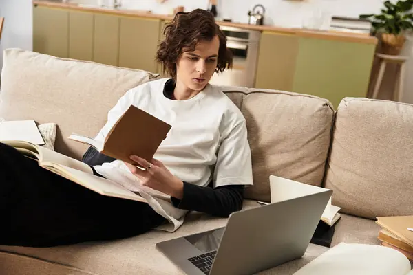 Young man relaxes in comfortable clothing, enjoying a blend of reading and online learning. — Fotografia de Stock