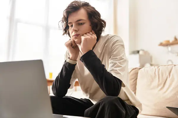 A young man sits comfortably at home, concentrating on his laptop while dressed in casual attire. — Foto stock