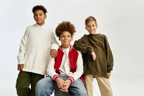 Tres adorables chicos llevan un atuendo elegante, sonriendo y posando alegremente juntos en un entorno brillante. - foto de stock