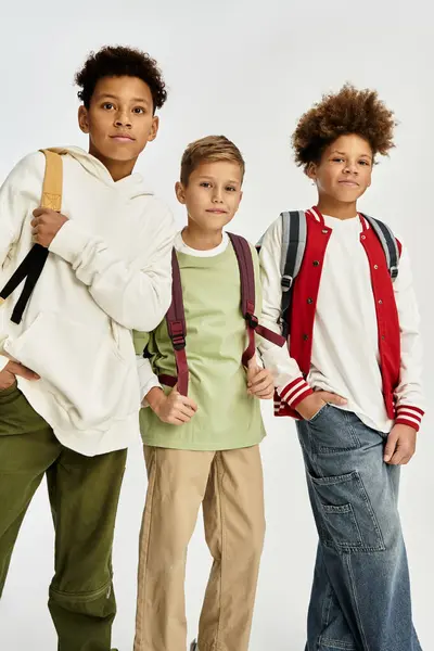 Tres adorables chicos vestidos con trajes de moda están de pie con confianza, compartiendo un momento alegre de amistad. - foto de stock