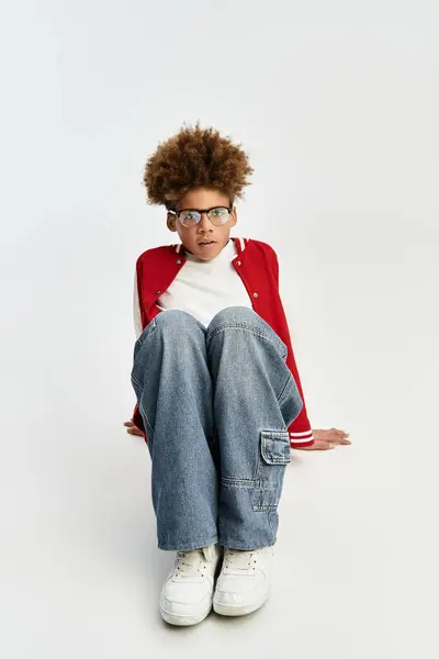 Adorabile ragazzo vestito con abiti colorati siede con fiducia con curiosità e stile all'interno. — Foto stock