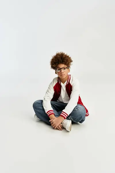 Adorable niño se sienta con las piernas cruzadas en un estudio brillante, mostrando su elegante atuendo. - foto de stock