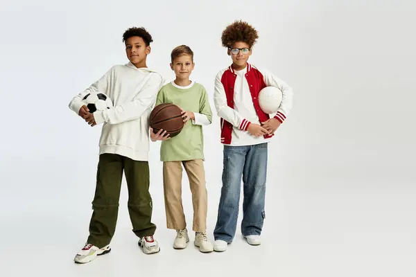 Los niños que usan trajes elegantes sostienen pelotas deportivas, celebrando su vínculo y amor por el tiempo de juego. - foto de stock