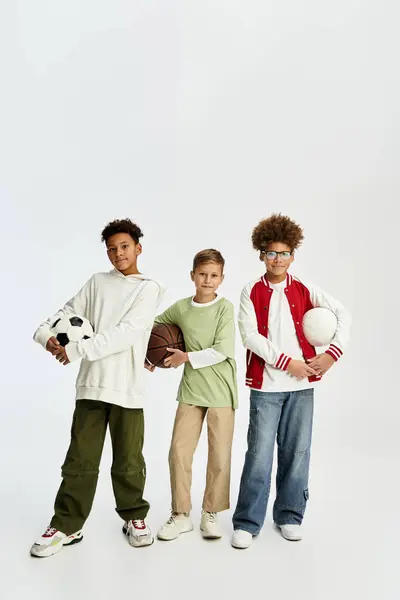 Three stylish boys stand together, joyfully holding sports balls. — Stock Photo