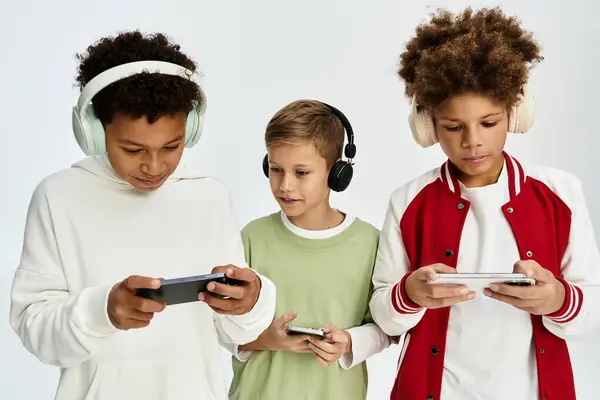 Three little boys in colorful outfits joyfully bond while playing games on their devices. — Stock Photo