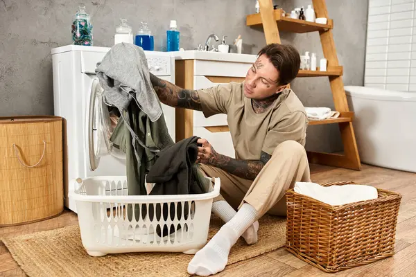 Ein junger, tätowierter Mann entspannt, während er zu Hause in einem gemütlichen, rustikalen Ambiente seine Wäsche sortiert. — Stockfoto