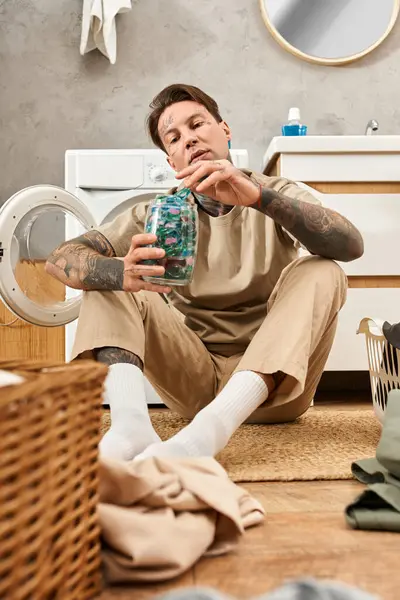 Junger Mann mit Tätowierungen entspannt zu Hause, sortiert Wäsche und engagiert sich in einem kreativen Projekt. — Stockfoto