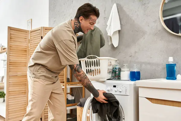 A young man with tattoos engages in laundry chores at his comfortable home, showcasing relaxation. — Stock Photo