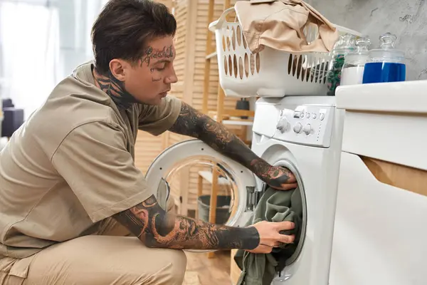 Junger Mann mit Tätowierungen geht Wäsche waschen, umgeben von einer angenehmen Atmosphäre zu Hause. — Stockfoto