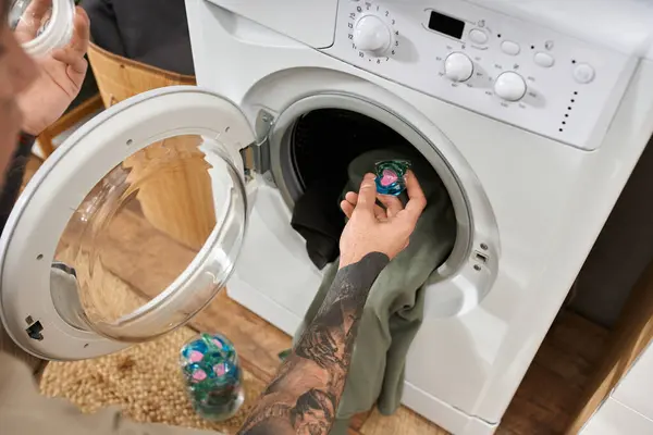 Handsome tattooed man enjoys a relaxing day at home while loading laundry into the washing machine. — Stock Photo