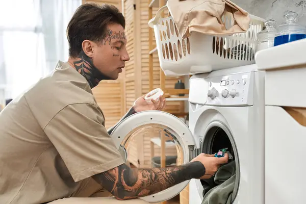 Tattooed young man enjoys a comfortable moment at home while doing laundry with care. — Stock Photo