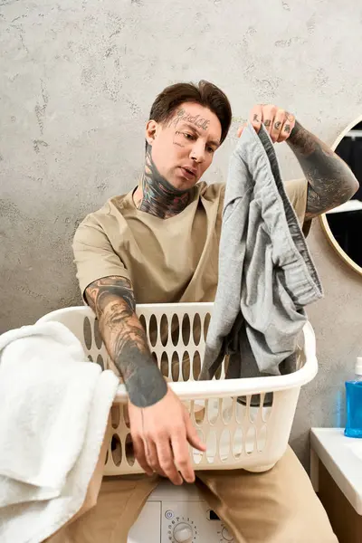 Handsome young man enjoys a comfortable moment at home, folding laundry with a playful attitude. — Stock Photo