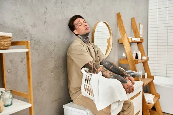 A tattooed young man relaxes in a cozy bathroom adorned with soft towels and natural decor. — Stock Photo