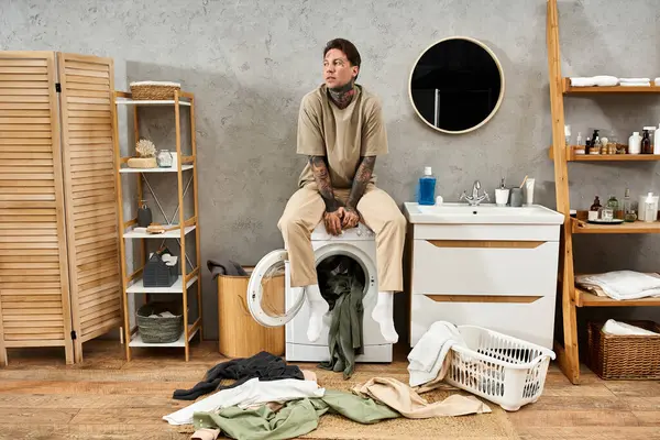 A handsome tattooed man takes a break while surrounded by laundry in a cozy home setting. — Stock Photo