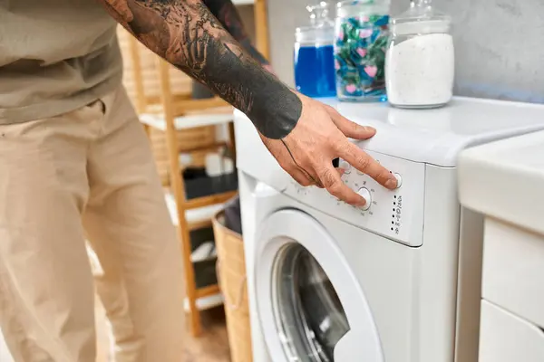 Tätowierter junger Mann startet die Waschmaschine und genießt Komfort und Leichtigkeit zu Hause. — Stockfoto