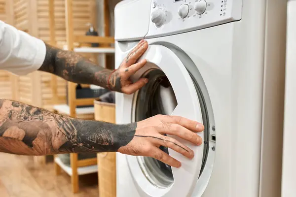 A young man with impressive tattoos engages in laundry chores at his comfortable home. — Stock Photo