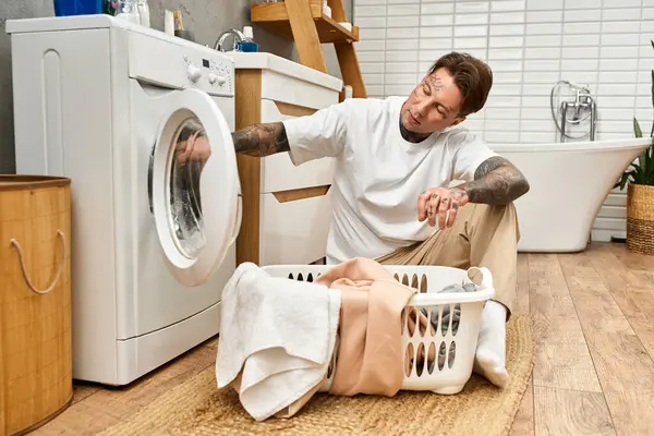 Tätowierter Mann wäscht Wäsche, während er sich in einem hellen, gemütlichen Badezimmer entspannt. — Stockfoto