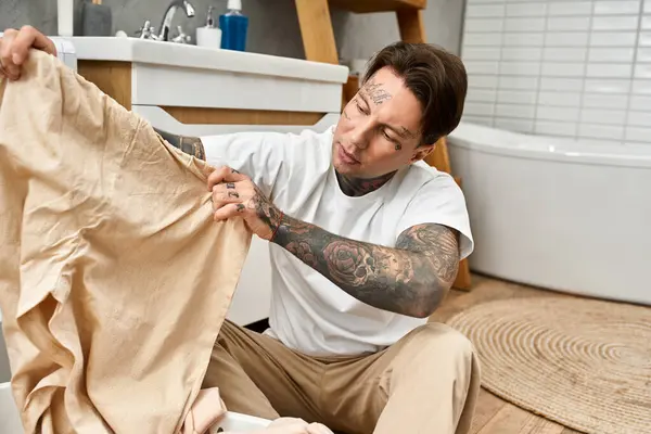 Junger Mann mit Tattoos faltet Wäsche in seinem gemütlichen Zuhause akribisch und verkörpert eine entspannte Atmosphäre. — Stockfoto