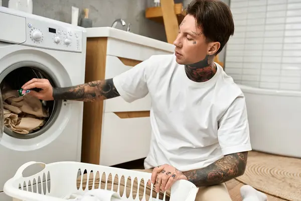 A young man with tattoos is actively doing laundry at home, creating a relaxed atmosphere. — Stock Photo