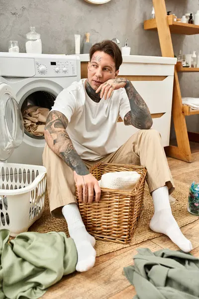 Ein junger Mann mit Tätowierungen entspannt zu Hause und sortiert Wäsche in gemütlicher Atmosphäre, umgeben von Wärme. — Stockfoto