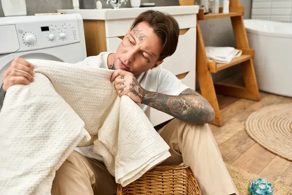 Ein tätowierter junger Mann faltet Handtücher in einer gemütlichen häuslichen Umgebung. — Stockfoto