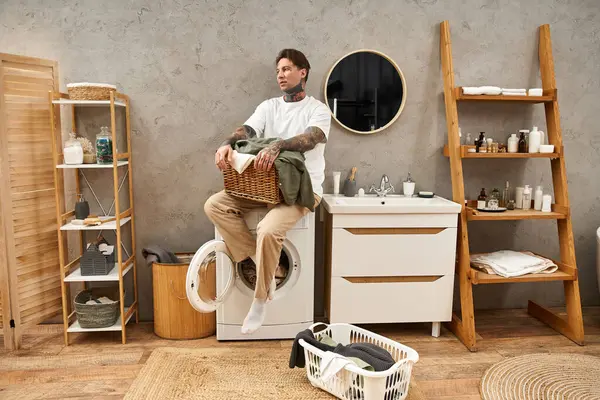 Ein junger tätowierter Mann sitzt gemütlich auf einer Waschmaschine, umgeben von einer gemütlichen Wohnatmosphäre. — Stockfoto