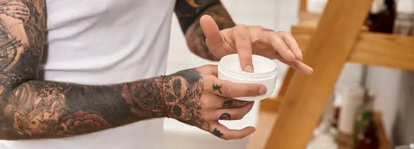 Ein junger Mann mit aufwändigen Tätowierungen in bequemer häuslicher Umgebung cremt seine Haut ein. — Stockfoto