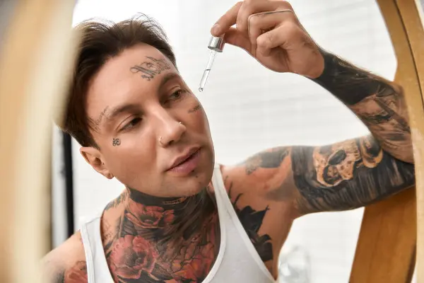 Ein tätowierter junger Mann trägt Serum auf seine Haut auf und genießt einen entspannten Moment zu Hause. — Stockfoto