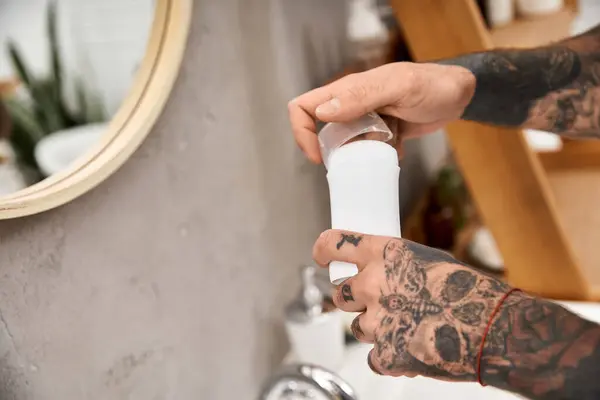 Hombre guapo tatuado aplica suavemente loción en un baño elegante y cómodo lleno de calidez. - foto de stock