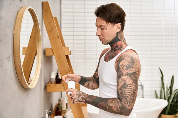 Ein junger Mann mit aufwändigen Tätowierungen steht in einem stilvollen Badezimmer und umarmt seine Selbstpflege-Routine. — Stockfoto