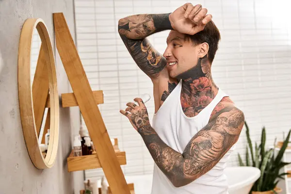 A tattooed young man smiles at his reflection in a cozy bathroom, exuding confidence. — Stock Photo