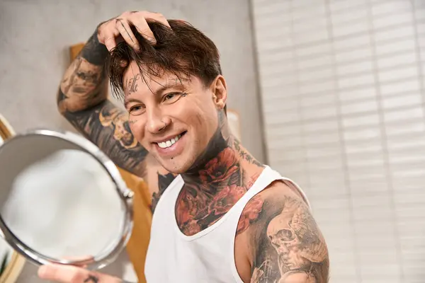 Un jeune homme tatoué sourit chaudement dans le miroir, ressentant de la joie dans sa maison confortable. — Photo de stock